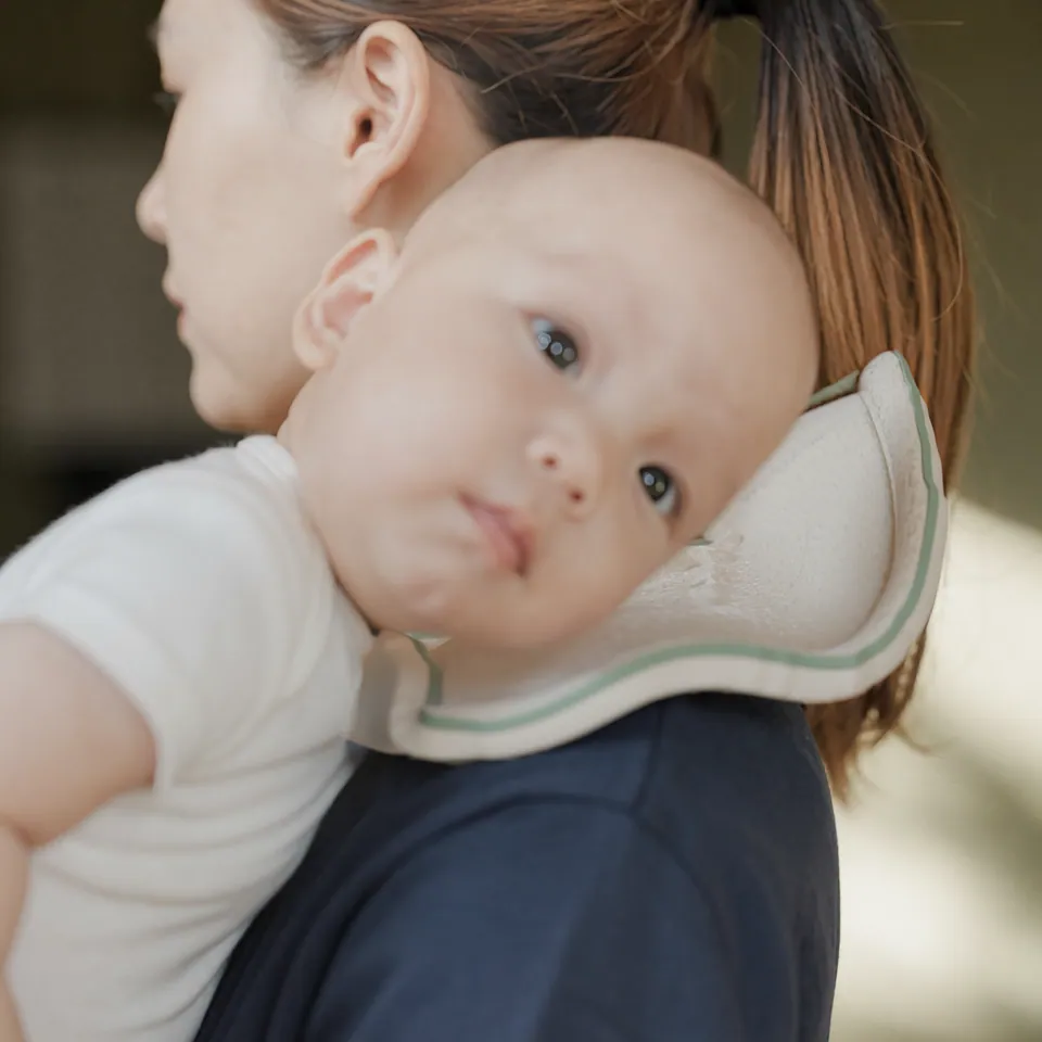 mybetterbib design visualization: a baby resting against mom’s shoulder, with the soft ivory shelf and sage rim beneath their cheek